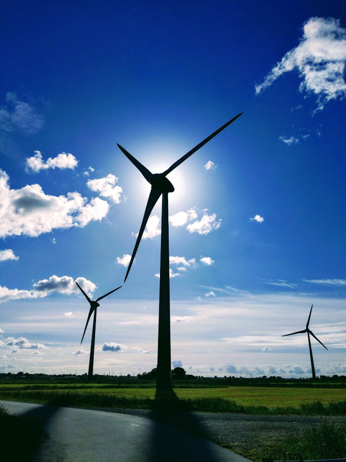 Photo of wind turbines silhouetted against a blue sky with clouds, symbolizing renewable energy.
